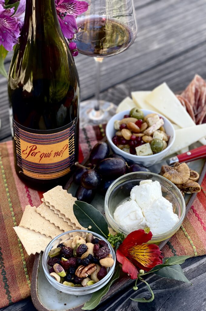 Charcuterie plate with cheese, crackers, nuts, meats displayed with a Por Que No wine bottle